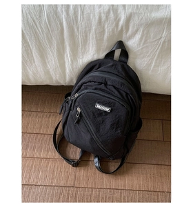 Detail of black nylon backpack featuring white MACHUGE logo tag and functional zipper pockets