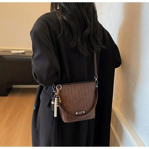 Detail of brown woven bucket bag featuring decorative wooden beads and a metal logo tag