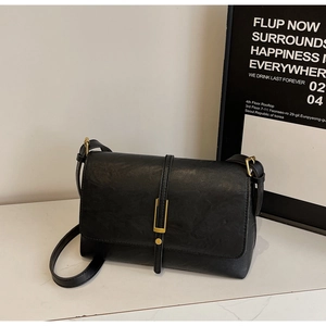 Close-up of black leather crossbody bag with elegant gold rectangular lock on marble top