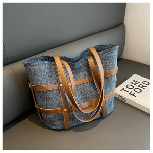 Detailed close-up of blue denim tote bag with brown leather straps and gold metal studs