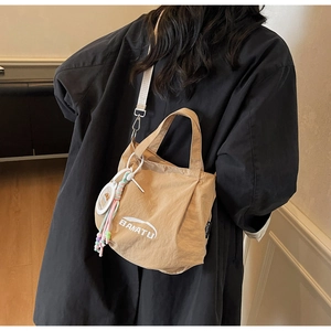 Detail of light brown nylon crossbody bag with white adjustable strap and cartoon charm