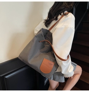 Dettaglio della grande borsa tote in tela grigia con manici in pelle marrone e logo