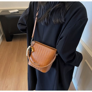 Detailed texture of brown woven bucket bag with beaded charm on model black coat
