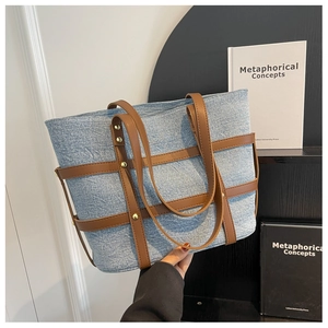 Detail of blue denim tote bag with red-brown leather handles and gold rivet studs