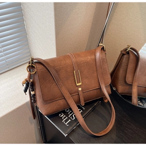 Detail of vintage brown shoulder bag featuring metallic gold buckle and wooden bead charm