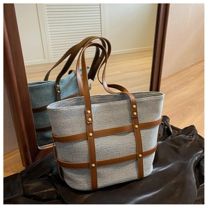 Detail of blue denim tote bag with brown leather trim and vintage gold rivets studs