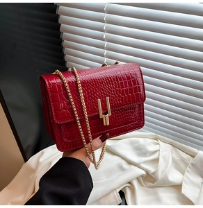 Close-up of deep red crocodile texture leather bag with gold chain and U-shaped metal lock