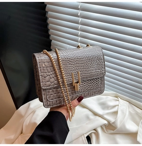 Detail of grey crocodile texture flap bag with elegant gold chain and metallic buckle