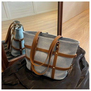Detail of blue denim tote bag featuring brown leather straps and gold stud accents