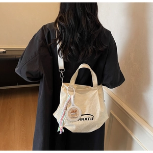 Detail of cream canvas tote bag featuring an ANATU logo and capybara charm accessory
