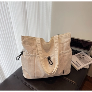 Detail of white nylon tote bag with drawstring pockets on a dark leather seat