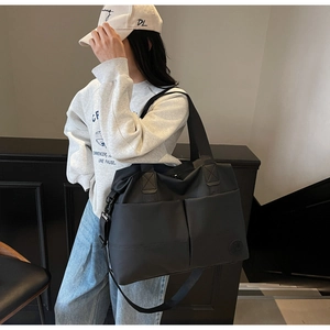 Detail view of a large black nylon tote bag with dual front pockets and shoulder strap