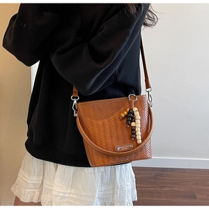 Detail of a brown woven texture bucket bag with a colorful beaded tassel charm