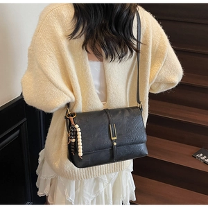 Detail of vintage black textured leather shoulder bag with gold clasp and bead charm