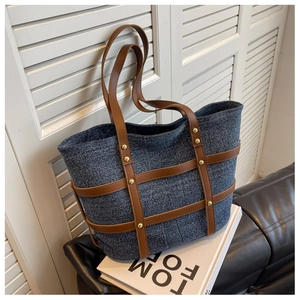 Detail of dark blue denim tote with brown leather stripes and gold rivet accents