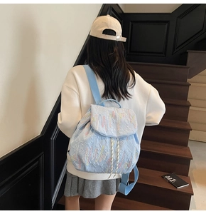 Detail of light blue quilted backpack with colorful wave embroidery worn by a model