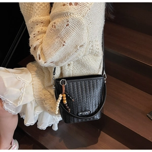 Detail of black woven bucket bag with beaded wooden charm and metallic brand tag