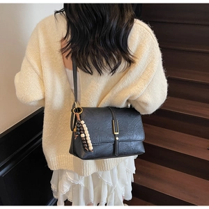 Détail du sac bandoulière rétro noir avec boucles dorées et breloque en perles
