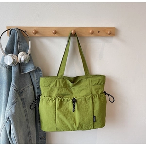 Detail of green nylon tote bag featuring functional outer drawstring pockets and durable fabric