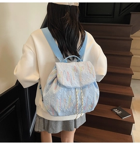 Detail of light blue quilted backpack with wavy embroidery worn by a model on stairs