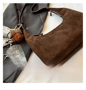 Close-up of vintage brown suede crescent bag with cute teddy bear charm on white linen