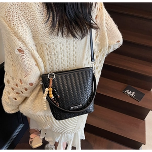 Detail of black woven bucket bag featuring wooden bead tassel and textured PU leather