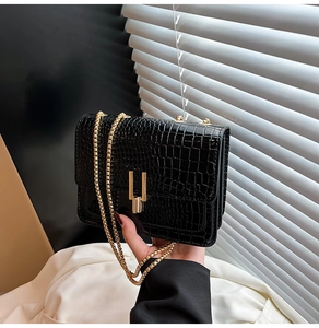 Close-up of black crocodile pattern leather with gold U-shaped metal buckle and chain