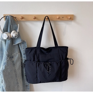 Detail of black nylon tote bag with drawstring pockets hanging on a wooden rack