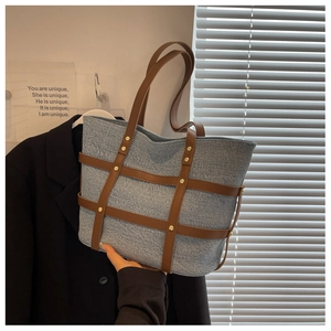 Detail of denim tote bag with brown leather crisscross straps and gold metal rivets