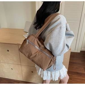 Close-up of brown nylon tote bag with metal zipper detail worn in lifestyle setting