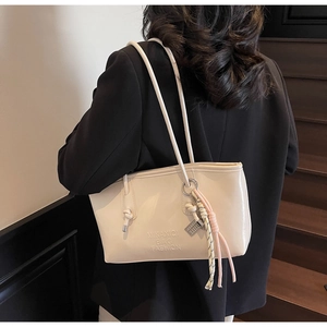 Detail of a large cream tote bag with embossed logo on a model in a black suit