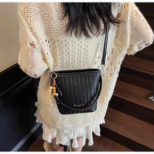 Detail of black woven bucket bag with wooden bead charm and thin shoulder strap