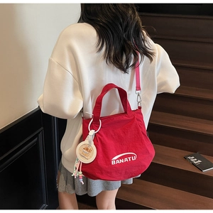 Detailed view of red canvas bucket bag with pink strap and capybara charm worn by model