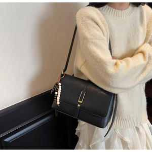 Close-up of black retro leather shoulder bag with decorative bead fringe and gold buckle