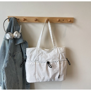 Detail of white nylon tote bag showing three front pockets with black drawstring closures