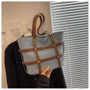 Detail of blue denim tote bag featuring brown leather straps and gold rivet embellishments