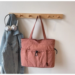 Close-up of pink nylon tote bag showing functional front pockets and drawstring detail