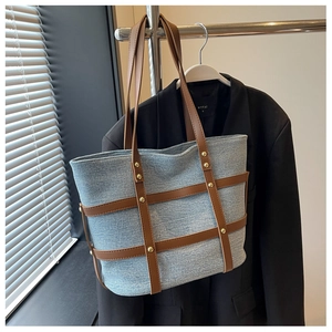 Detail of blue denim tote bag with brown leather straps and gold stud accents