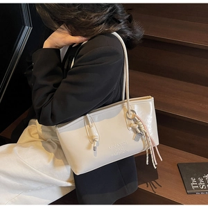 Close-up of cream PU leather tote bag with embossed logo and colorful braided charm