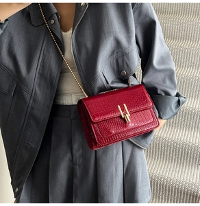 Detail view of red crocodile embossed leather bag with gold chain strap on a model