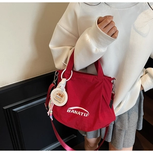 Detail of red nylon hobo bag with Banatu logo and cute capybara pendant on a model