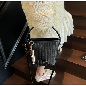 Detail of black woven bucket bag with beaded charm and adjustable strap on a model