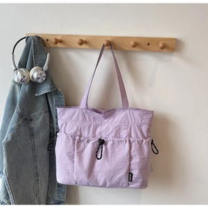Detail of lavender nylon tote bag with drawstring side pocket and brand label on wall hook