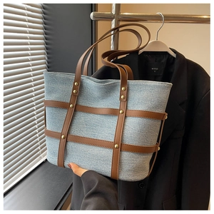 Close-up of denim tote bag featuring brown leather straps and gold rivet detailing