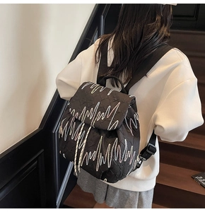 Detail of black quilted backpack featuring contrast white wave embroidery and flap design
