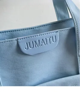 Detailed close-up of light blue tote bag featuring embossed logo on leather patch