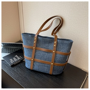 Detailed macro view of denim tote bag featuring brown leather straps and gold rivets