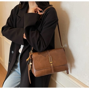 Brown vintage flap bag with gold clasp and bead charm shown on model in black blazer