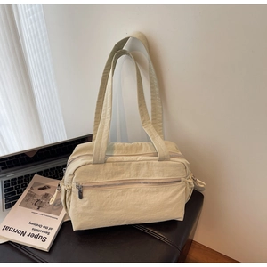 Close-up of a cream nylon shoulder bag featuring dual zippers and a front pocket