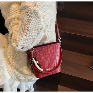 Detail of red woven bucket bag with distinctive wooden bead tassel on knit sweater